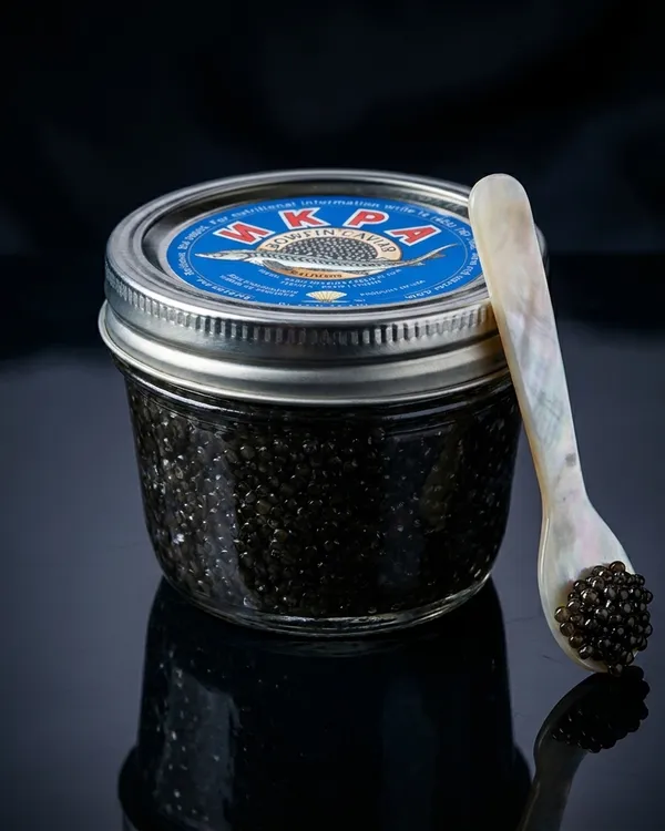 A jar of Bowfin caviar, naturally true-black roe, on dark slate.