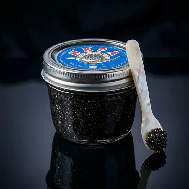 A jar of Bowfin caviar, naturally true-black roe, on dark slate.